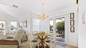 Ein helles Wohnzimmer mit einem Esstisch, Korbstühlen, einer Couch und einer Deckenleuchte.