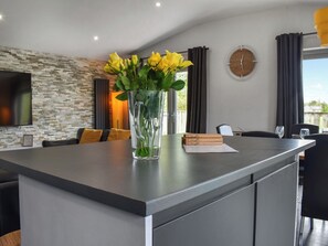 Uma cozinha moderna com uma ilha central, um vaso com flores amarelas e uma área de jantar com cadeiras e uma mesa.
