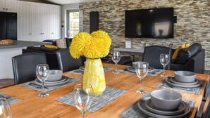 A modern dining area with a wooden table set for six, surrounded by black leather chairs. A yellow vase with flowers is placed in the center.