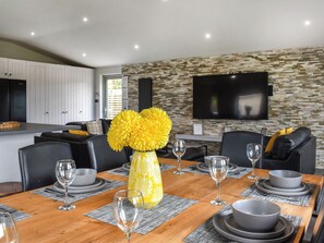 Un espace repas moderne avec une table en bois dressée pour six personnes, entourée de chaises en cuir noir. Un vase jaune rempli de fleurs est placé au centre.