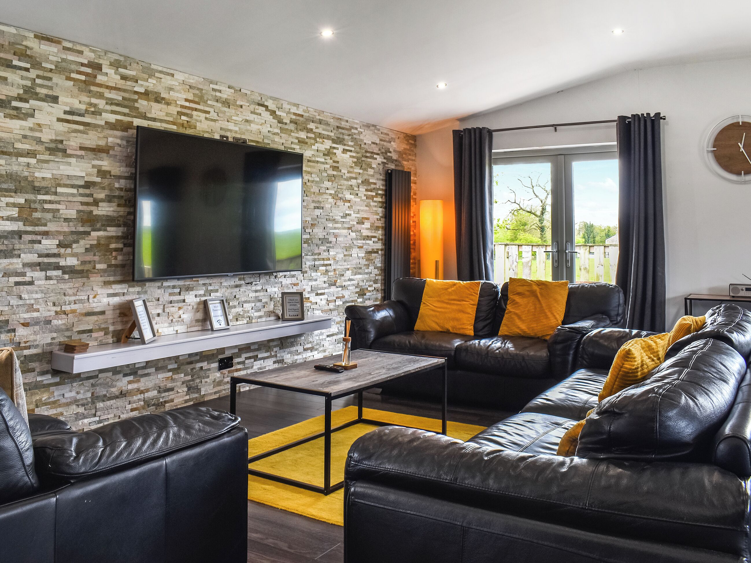 A modern living room with a stone wall, leather sofa, and a flat-screen TV.