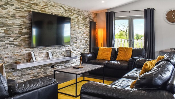 A modern living room with a stone wall, leather sofa, and a flat-screen TV.