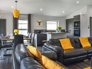 Uma sala de estar moderna com um sofá de couro preto, almofadas amarelas e uma área de jantar com mesa e cadeiras de madeira.