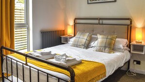 A neatly made bed with a yellow throw blanket, two bedside lamps, and a painting on the wall.