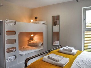 Une chambre avec un lit superposé, une table de chevet, un miroir et une fenêtre avec des stores.