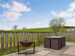 A patio with a metal grill, wicker furniture, and a wooden fence.