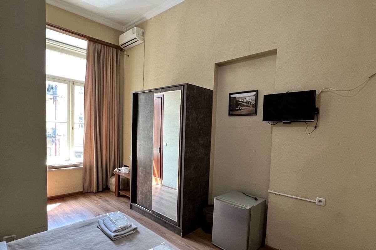 A hotel room with a bed, a wardrobe, a television, and a small trash bin.