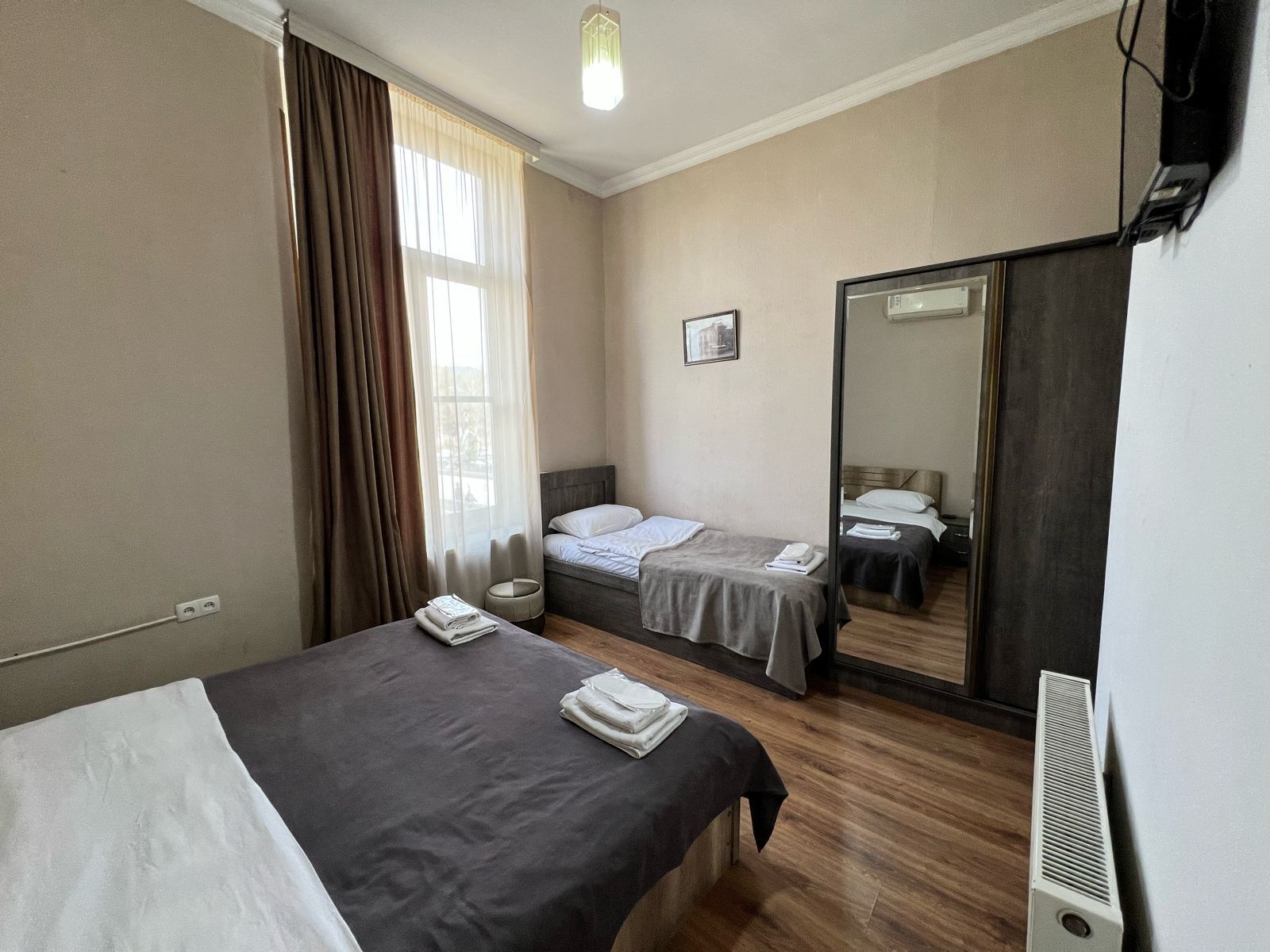 Una habitación de hotel con dos camas individuales, un espejo grande, un calentador y una ventana con cortinas.