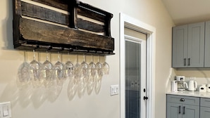A kitchen with a built-in wine rack holding several wine glasses, a door with a window, and grey cabinets. - Experience the Ultimate Getaway at Our Stunning Riverfront Property!!! (St. Joseph)