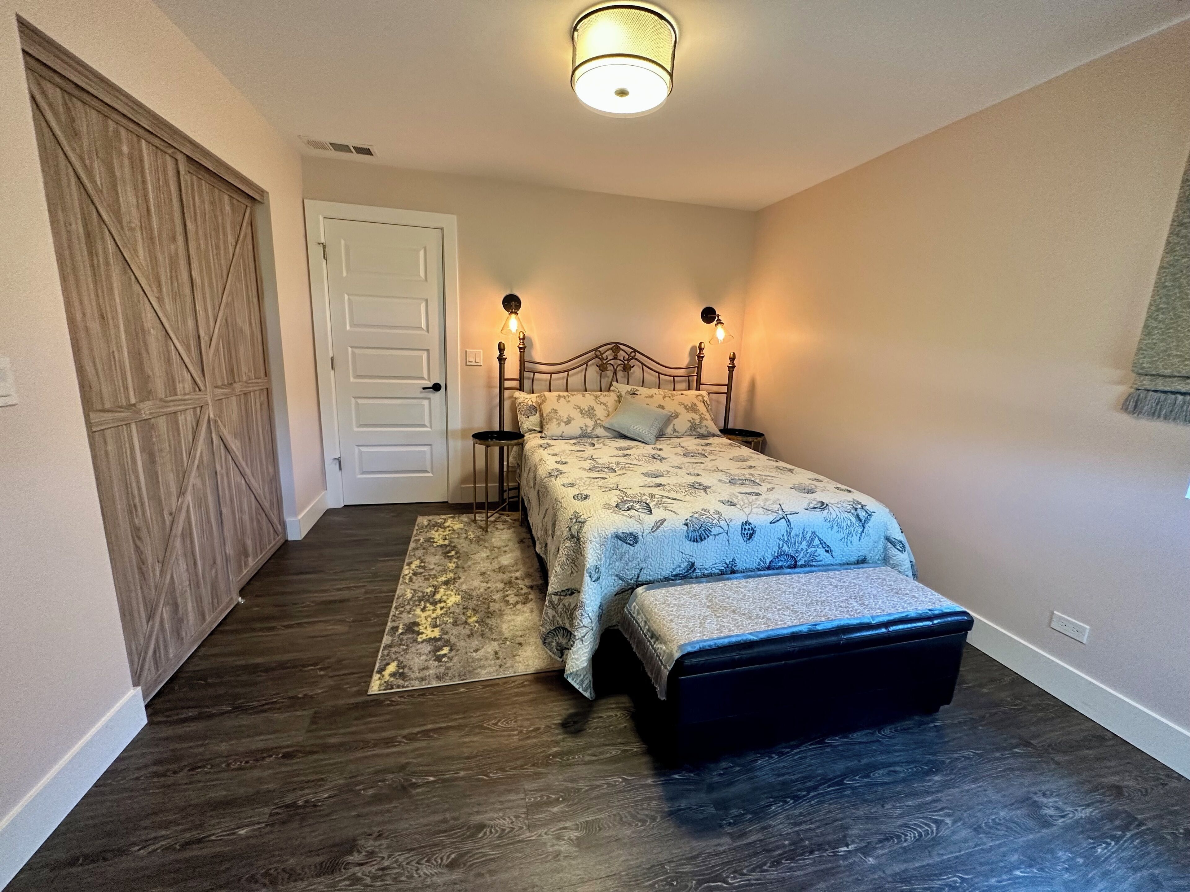A bedroom with a bed, bedside tables, a bench, a door, and a ceiling light.