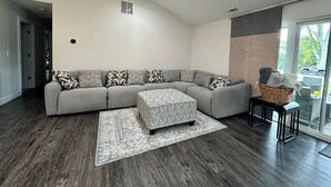 A modern living room with a grey sectional sofa, patterned throw pillows, a matching ottoman, and a woven basket on a side table. - Experience the Ultimate Getaway at Our Stunning Riverfront Property!!! (St. Joseph)
