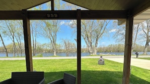 A covered outdoor seating area with wicker furniture, overlooking a grassy lawn and a body of water. - Experience the Ultimate Getaway at Our Stunning Riverfront Property!!! (St. Joseph)