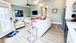 Una cocina moderna con una isla central, muebles blancos y un comedor con sillas de madera.