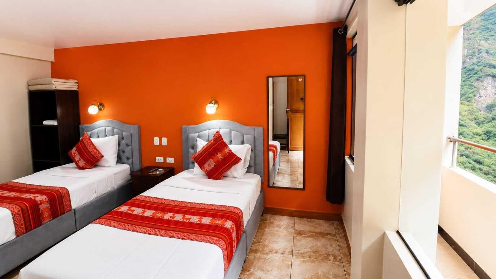 A hotel room with two beds, a large mirror, and a view of a mountainous landscape.