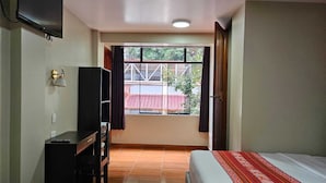 A hotel room with two beds, a desk, a TV, and a window with a view of the outside. - Hotel Horizonte (Machu Picchu)
