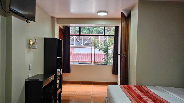 A hotel room with two beds, a desk, a TV, and a window with a view of the outside. - Hotel Horizonte (Machu Picchu)