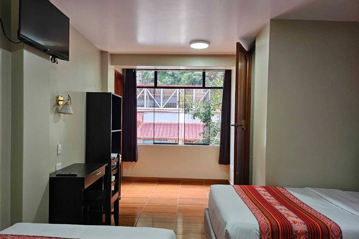 Une chambre d’hôtel avec deux lits, un bureau, une télévision et une fenêtre donnant sur l’extérieur.