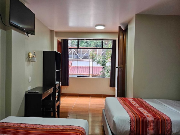 A hotel room with two beds, a desk, a TV, and a window with a view of the outside. - Hotel Horizonte (Machu Picchu)