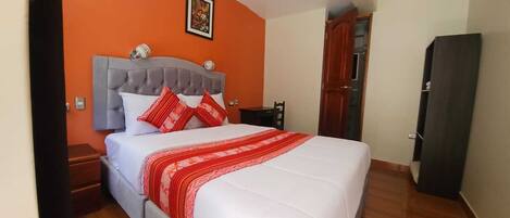 Quarto com cama, mesa de cabeceira, guarda-roupa de madeira e parede laranja.