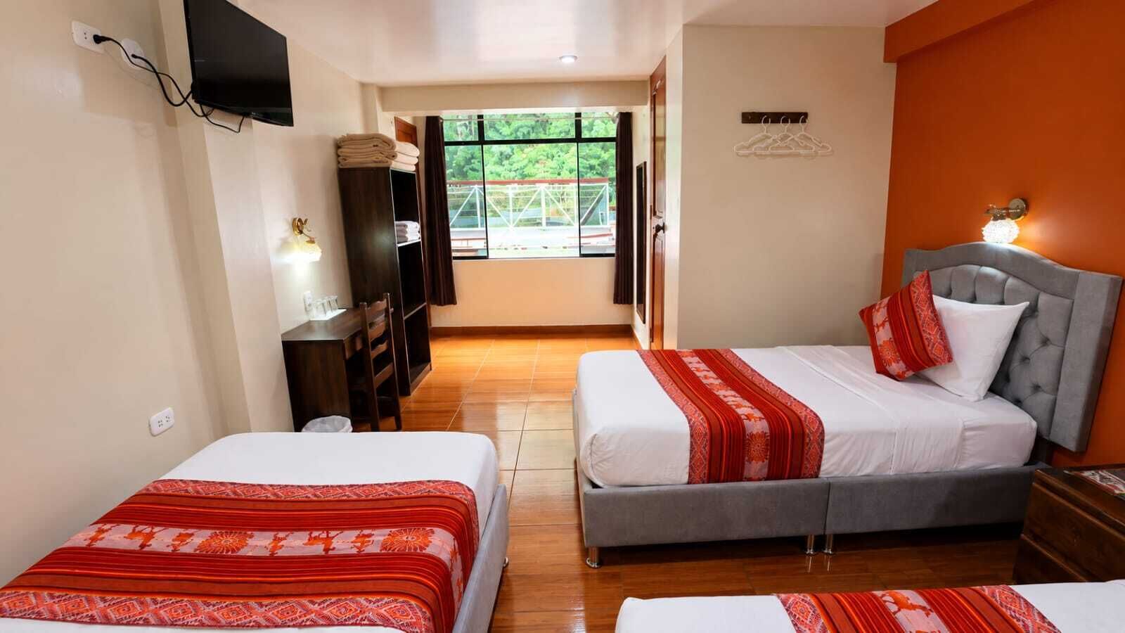 Habitación de hotel con dos camas, un escritorio, una silla, un televisor y vistas al exterior.