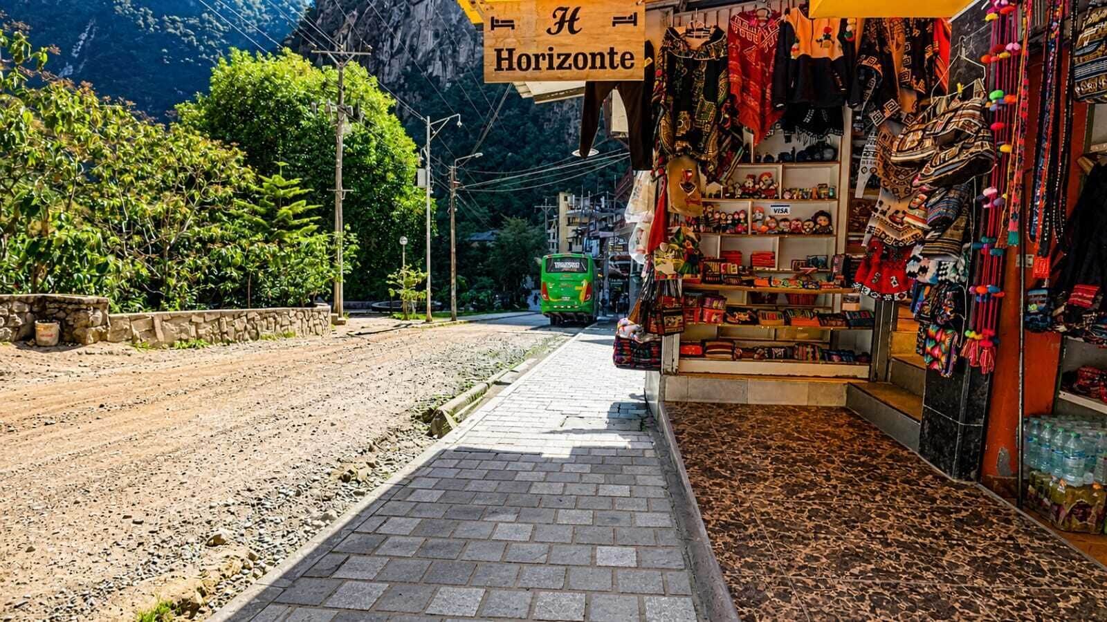 Una calle con una tienda a la derecha que exhibe varios artículos.