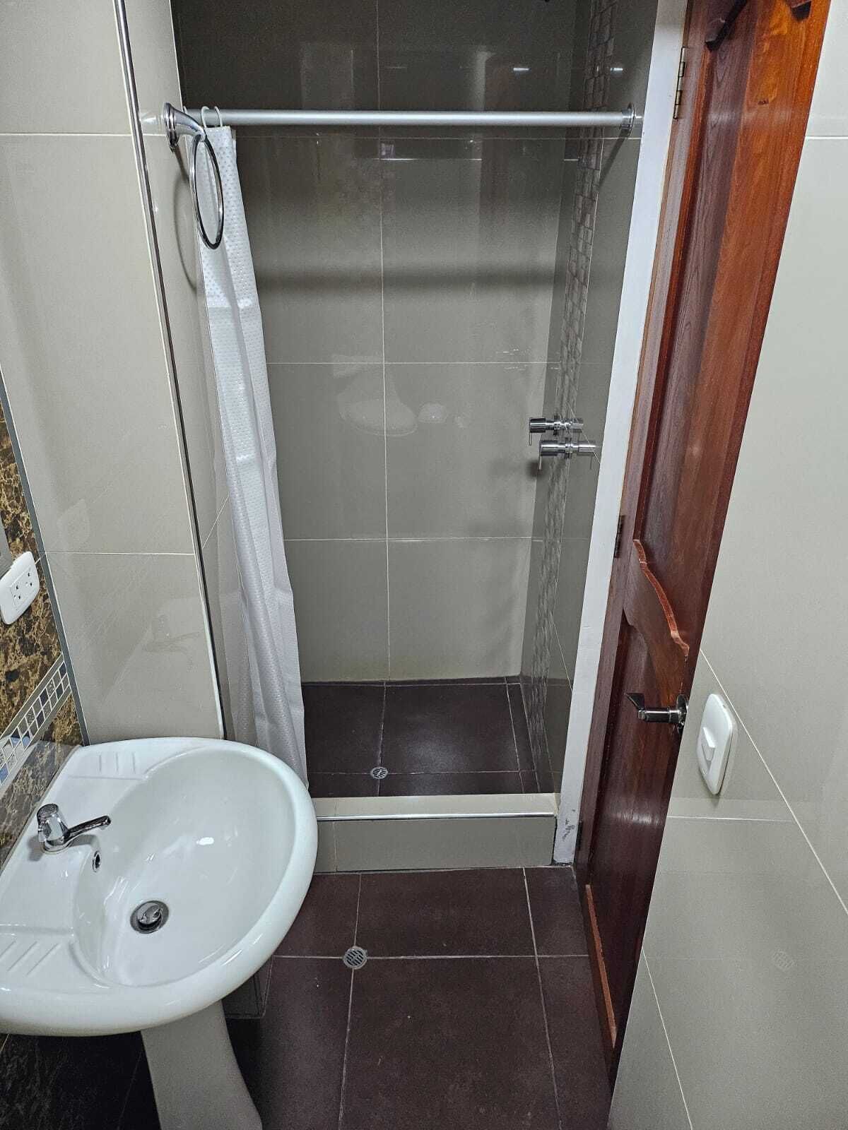 Un bany amb dutxa, un lavabo i una porta de fusta.