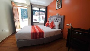 A bedroom with a bed, a chair, and a window with a view of buildings. - Hotel Horizonte (Machu Picchu)