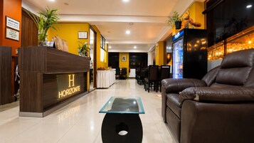 Un hall de hotel con una mesa de recepción, una zona de estar y un espacio para comer.