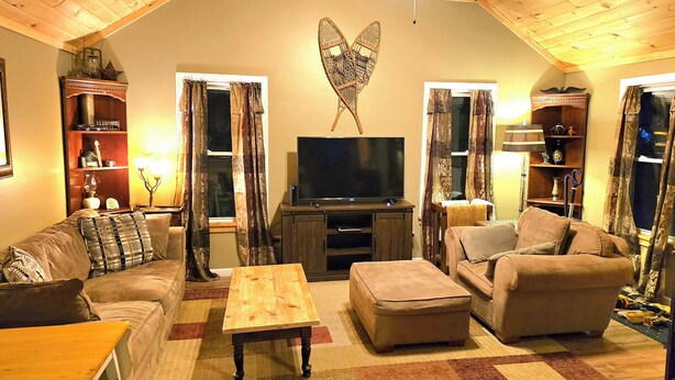 Ein gemütliches Wohnzimmer mit Fernseher, Sofas, einem Couchtisch und einer dekorativen Engel-Wandskulptur.