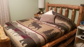 Ein hölzernes Bett mit einem gemusterten Überwurf und Kissen, eine Nachttischlampe und ein kleiner Nachttisch mit einer Kerze.