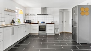 A modern kitchen with white cabinets, a black tiled floor, a stainless steel refrigerator, and a built-in oven.