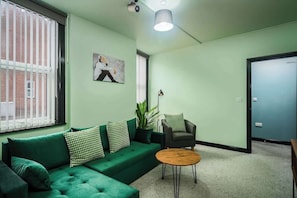 Ein Zimmer mit einem grünen Sofa, einem runden Holztisch, einem schwarzen Sessel und einem Gemälde an der Wand.