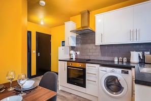 A compact kitchen with a washing machine, oven, and a coffee maker.