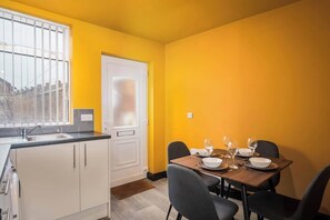 Een eetgedeelte met een tafel voor vier personen, een raam met metalen tralies en een witte deur.