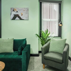 Een kamer met een groene bank, een grijze fauteuil en een grote groene plant.