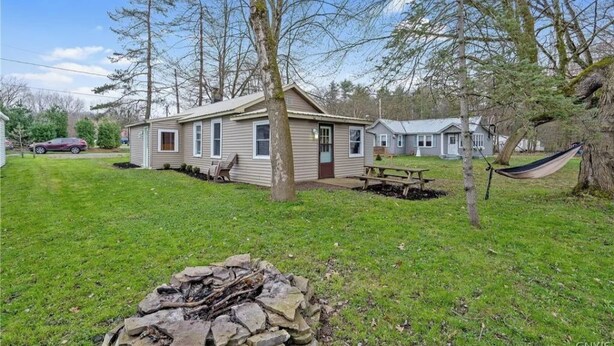 A single-story house with a front yard, a stone fire pit, and a hammock.