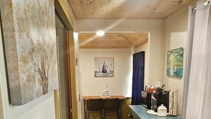 A narrow hallway with a wooden floor, a table with chairs, and a blue cabinet.