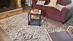 A cozy living room with a stone fireplace, a red sofa, a wicker chair, and a patterned rug.