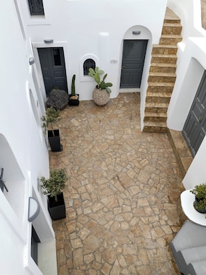 A courtyard with stone flooring, white walls, and a stone staircase. - The Lithos Villa | The Perfect retreat to enjoy the immense beauty of Santorini (Thira)