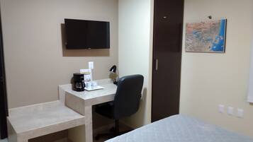 Une chambre d’hôtel équipée d’un lit, d’un bureau avec une chaise, d’une télévision, d’une machine à café et d’une carte affichée au mur.