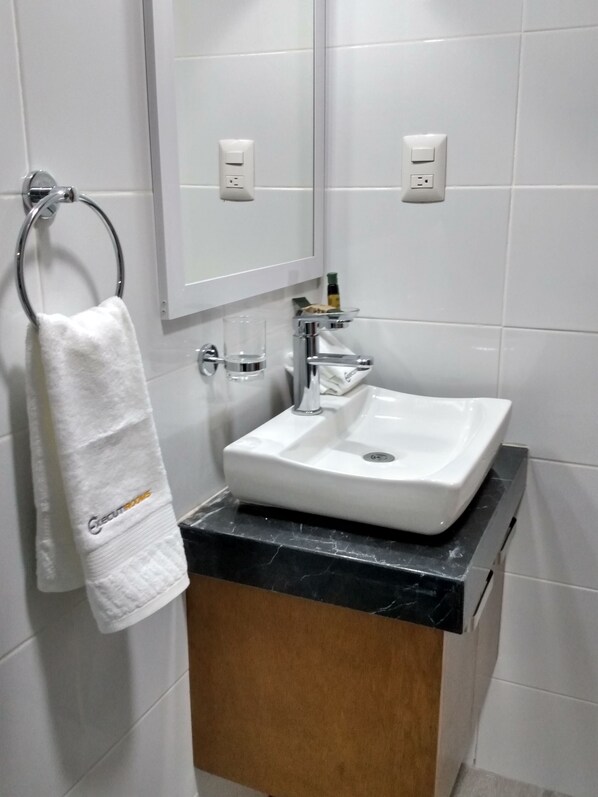 A bathroom with a white sink, a towel rack with a white towel, a mirror above the sink, and a wooden cabinet below.