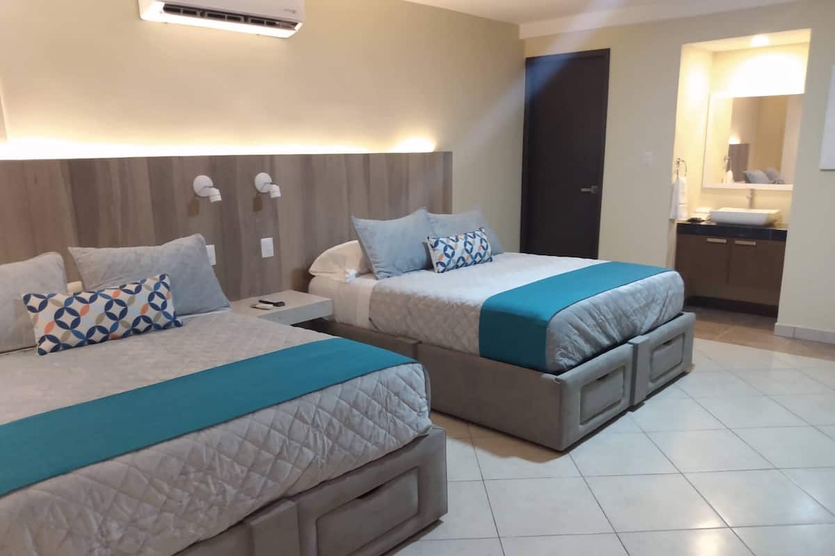 A hotel room with two beds, a small bedside table, a nightstand, a built-in wardrobe, and a bathroom with a sink and mirror.