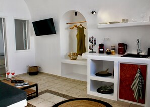 A modern living room with a flat-screen TV, a coffee machine, a sink, and a dining area with a table and chairs.