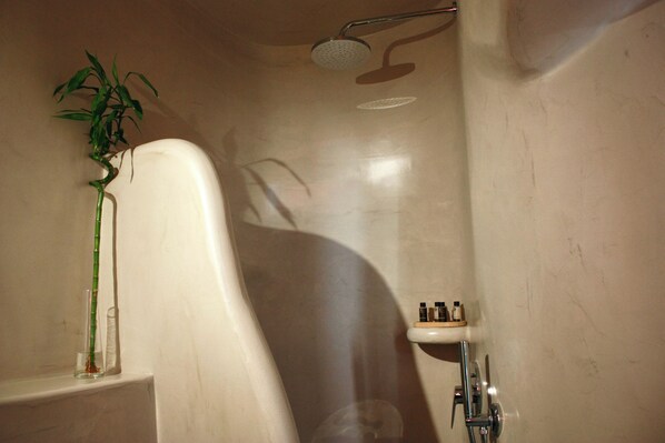 A bathroom with a bathtub, a showerhead, a shelf with toiletries, and a bamboo plant.