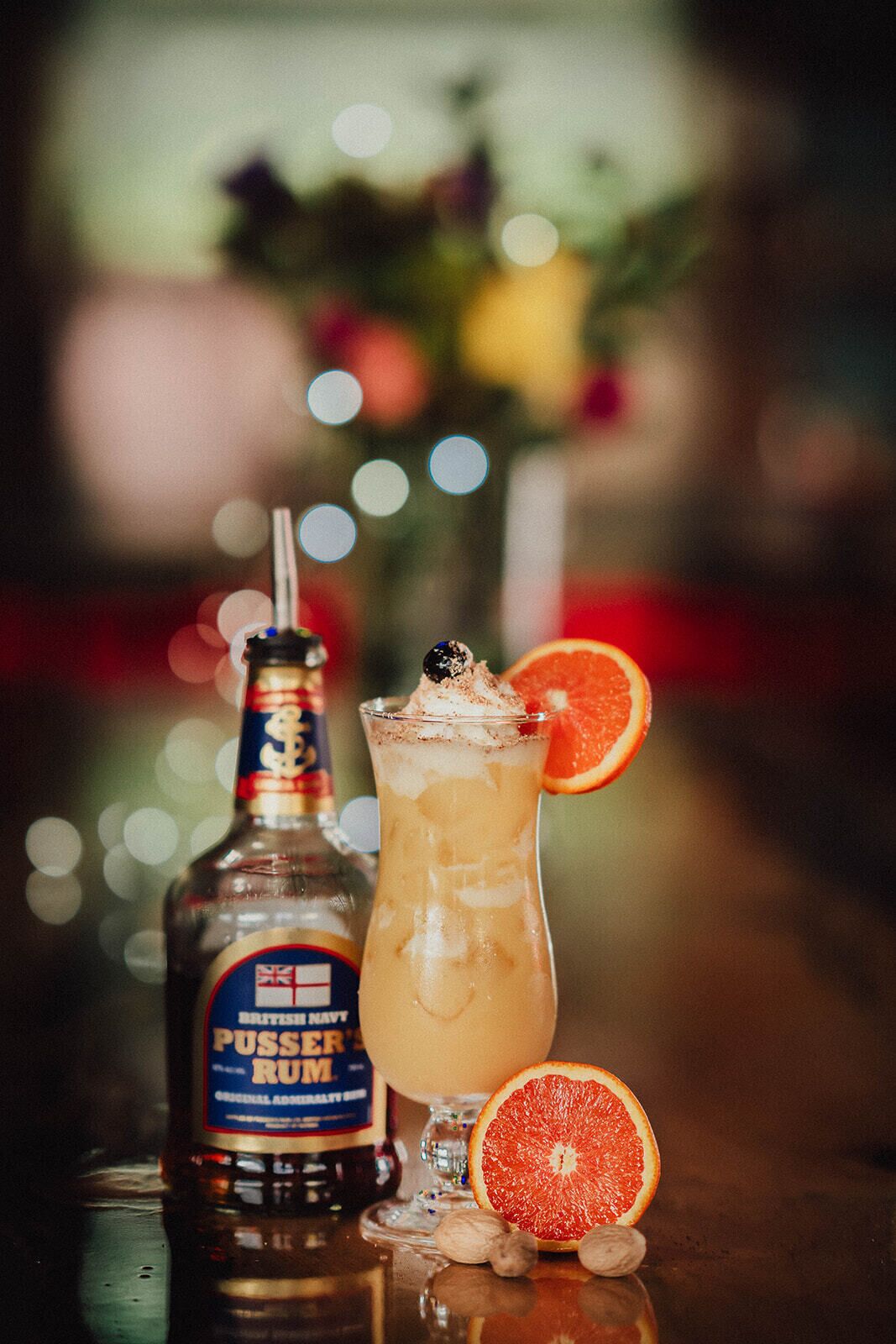 Une bouteille de rhum britannique de la marque Pusser's, ainsi qu'un cocktail agrémenté d'une tranche de pamplemousse et d'une paille.