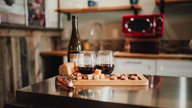 A wooden cutting board with cheese, nuts, and bread on a kitchen counter. - MyFarm Stay/Rustic Barn Charm with Modern Comforts/walk to dining. Pet-Friendly! (Merlin)