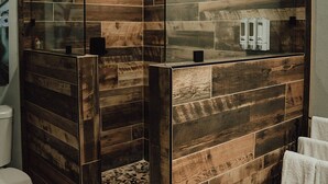 A modern bathroom with wooden paneling, a glass shower enclosure, and a pebbled floor. - MyFarm Stay/Rustic Barn Charm with Modern Comforts/walk to dining. Pet-Friendly! (Merlin)
