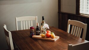 A dining table with chairs, a bottle of wine, a can of beer, and a fruit tray. - MyFarm Stay/Rustic Barn Charm with Modern Comforts/walk to dining. Pet-Friendly! (Merlin)