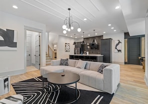 A modern living room with a sectional sofa, a round coffee table, and a kitchen in the background. - New Lakeside Home w/kayaks, Game Room, Billiards (Winchester)