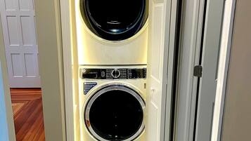 A laundry room with two front-loading washing machines, a control panel, and a door leading to another room.